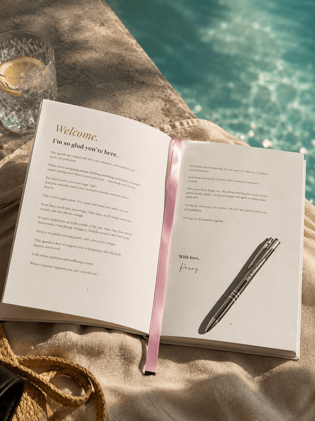 Open book with a pen and pink ribbon on a surface near a pool, reading the Welcome Letter from Penny, the author.