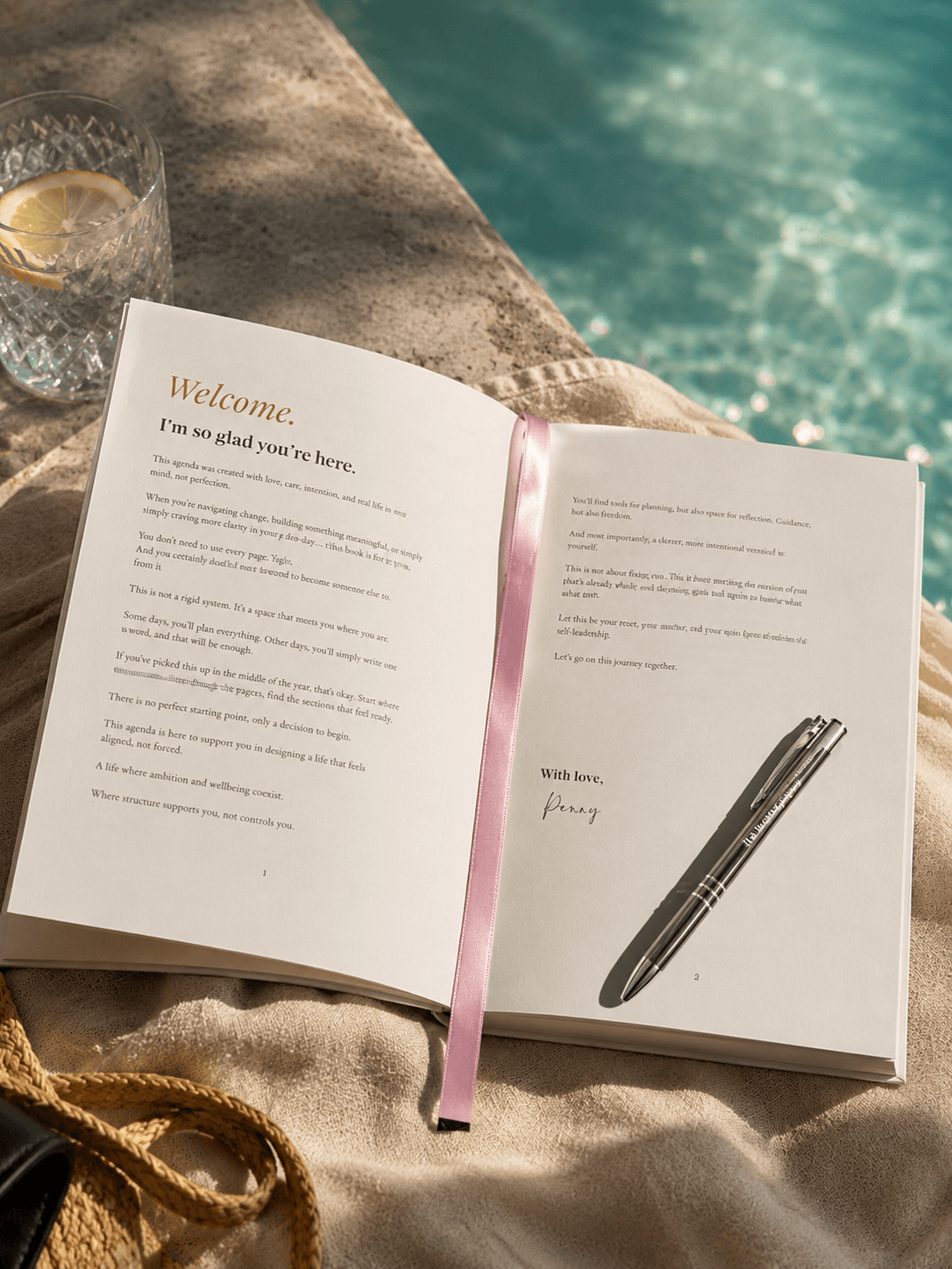 Open book with a pen and pink ribbon on a surface near a pool, reading the Welcome Letter from Penny, the author.